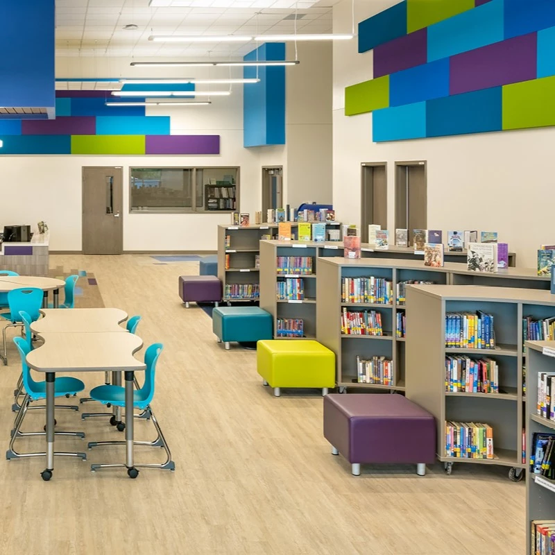 Institutional library media center with shared tables, task chairs, low shelving and soft seats