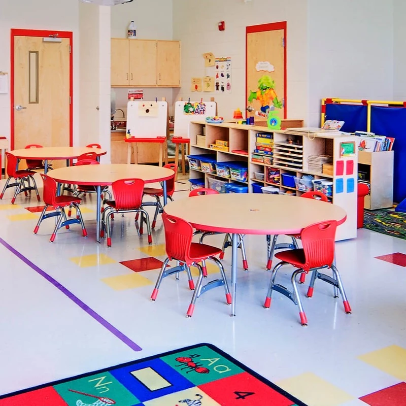 Early-learning classroom with child-scale round tables, red chairs and open storage